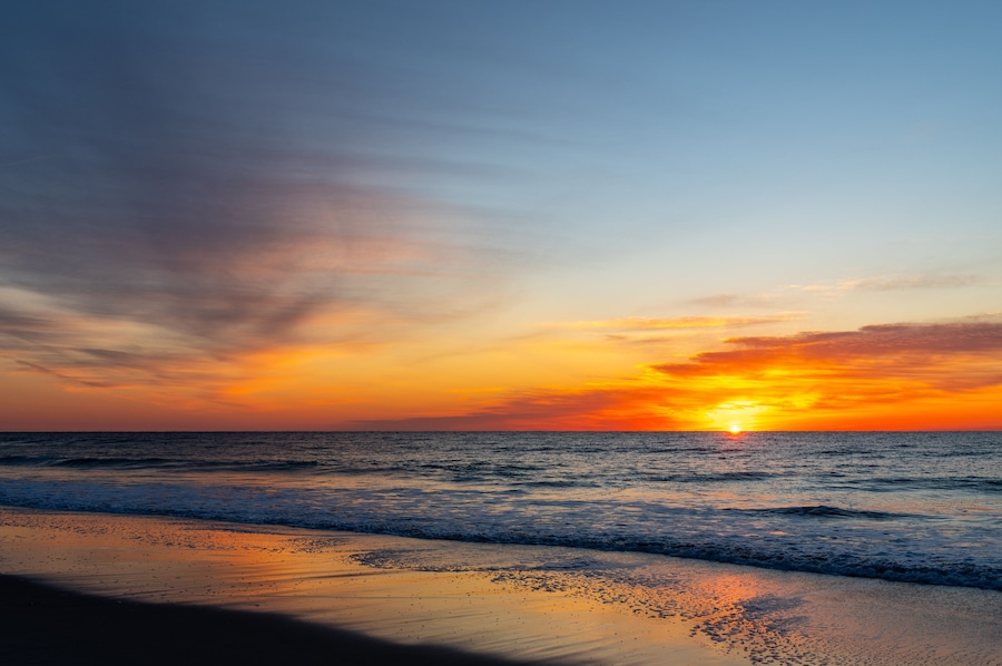 Atardecer sobre el océano con una playa al frente.