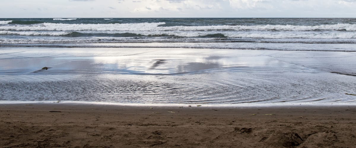 A beach with waves, sand, and a cloudy sky.
