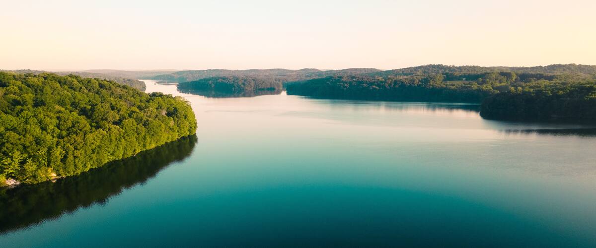 A calm lake surrounded by dense forest and hills.