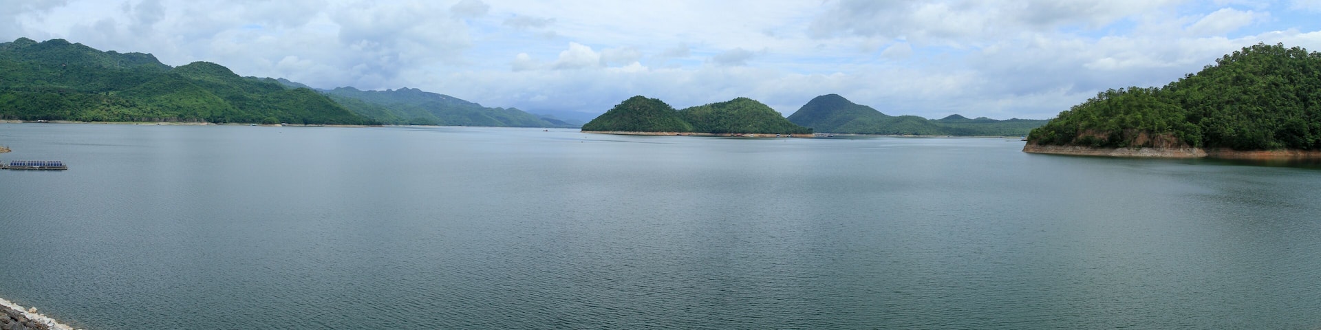 Un lago tranquilo rodeado de colinas verdes exuberantes y un cielo parcialmente nublado.