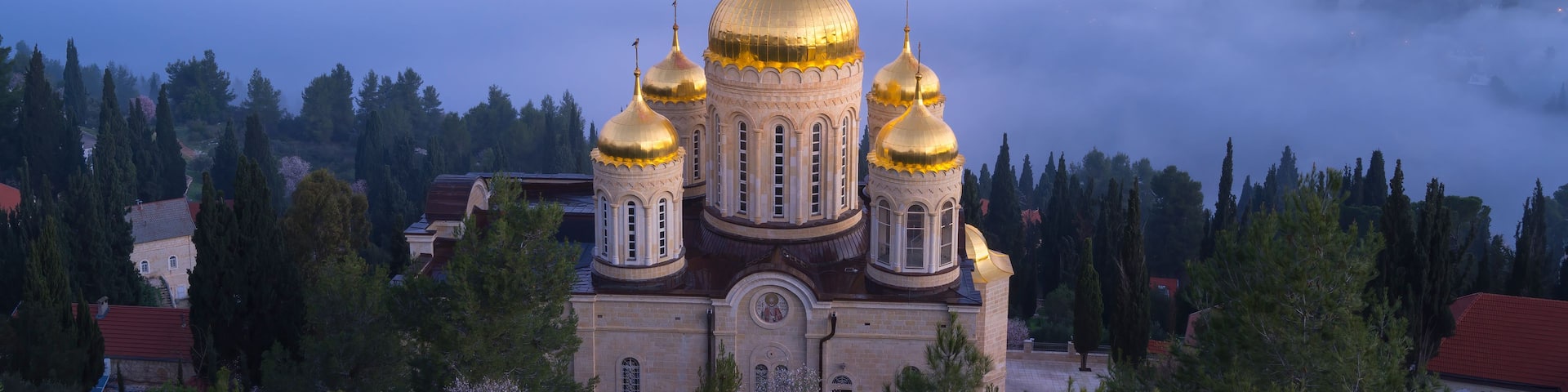 A church with golden domes surrounded by trees and fog.