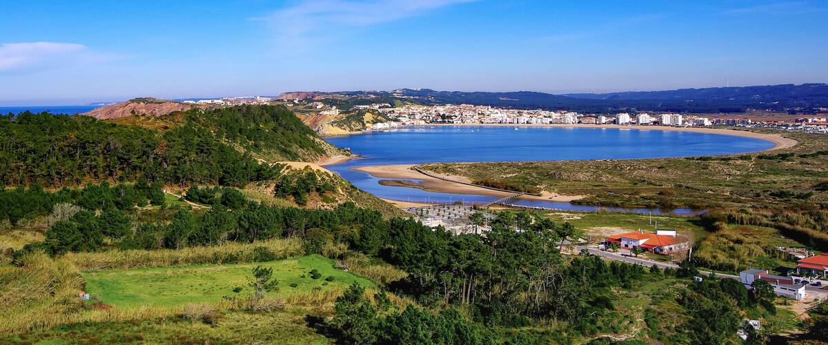 A coastal town with a bay, green hills, and a clear blue sky.