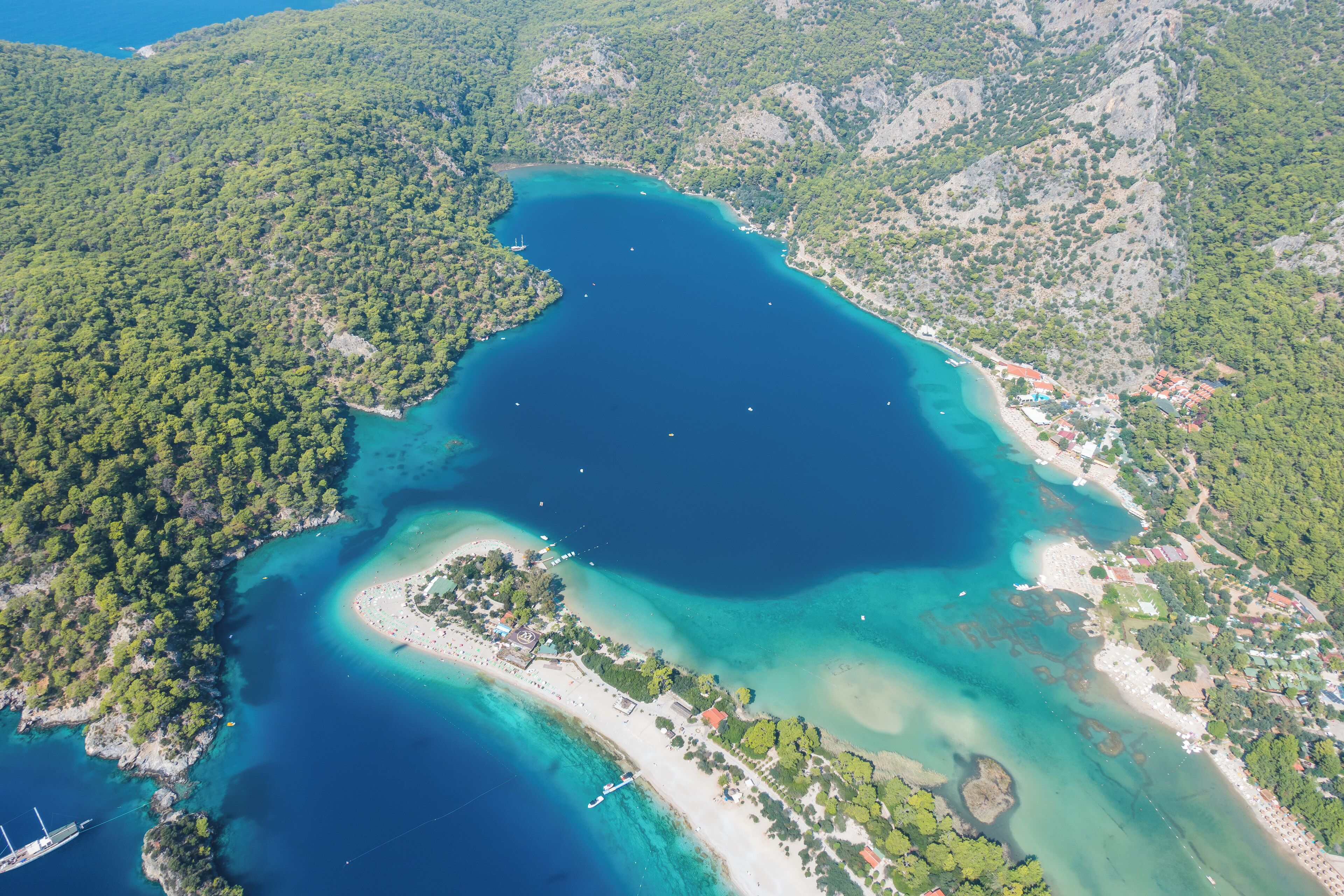 An aerial view of a coastal area with a large bay, a small island, and a beach with buildings.