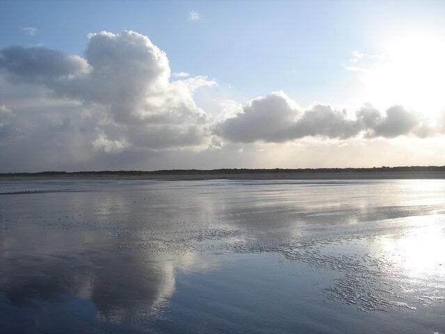 A beach with wet sand and a cloudy sky.