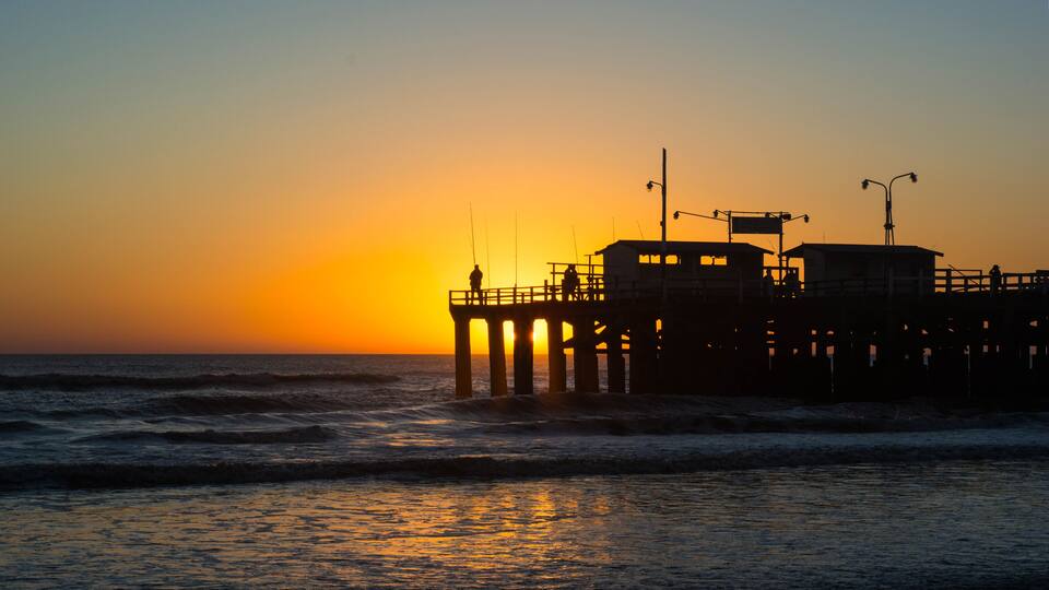 A pier at sunset with the sun setting over the ocean.