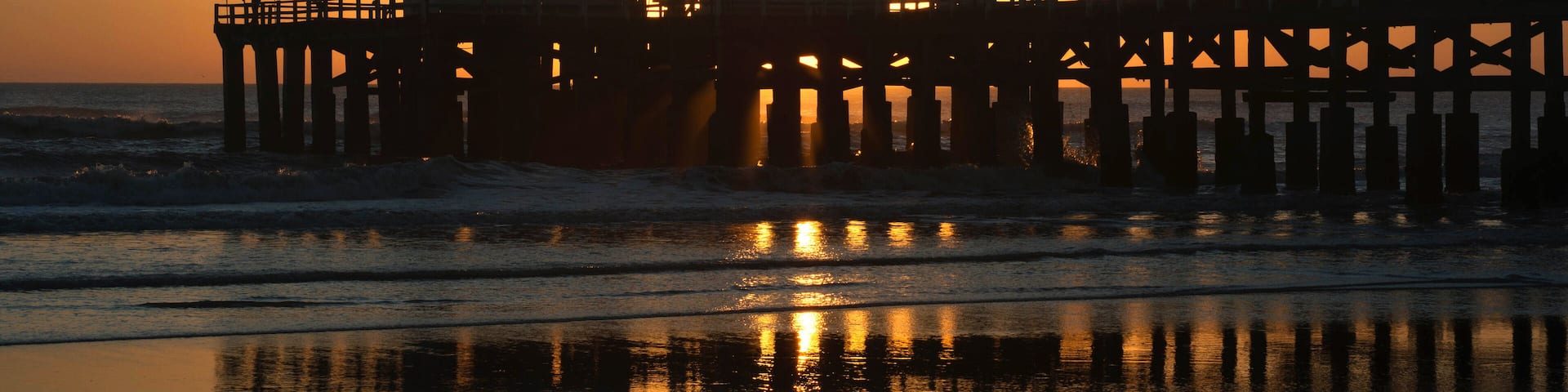 A pier at sunset with reflections on the water.
