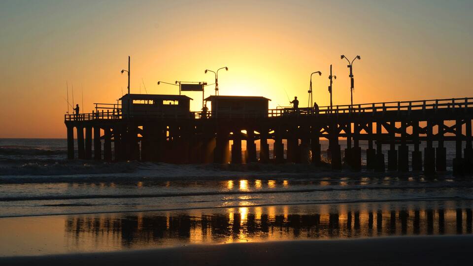 A pier at sunset with reflections on the water.