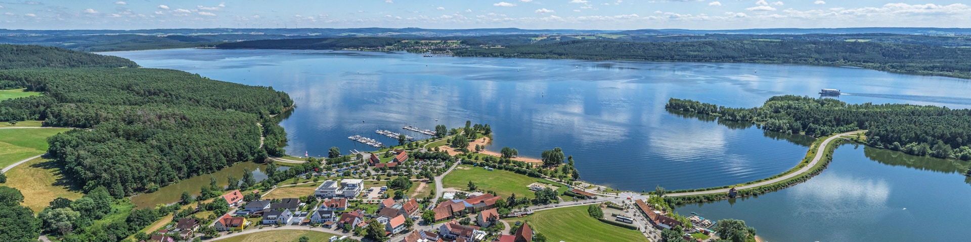 Ein Dorf am See mit Häusern, Stegen und blauem Himmel.
