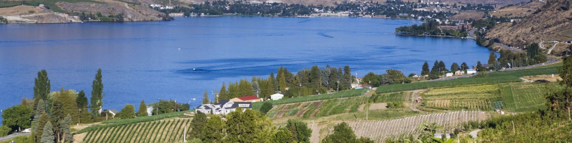 Un lago rodeado de colinas, viñedos y pequeñas construcciones.