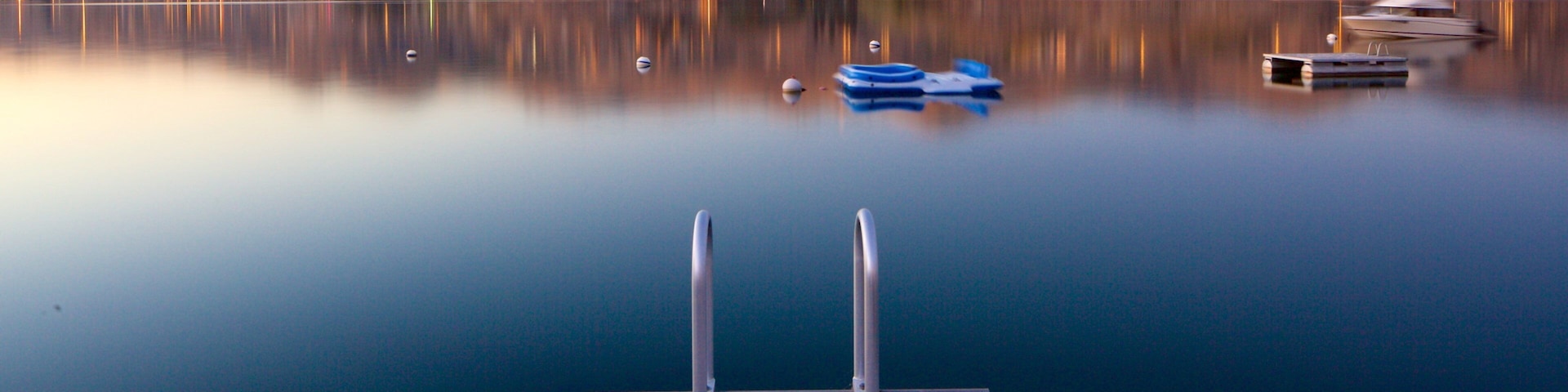 A calm lake with a wooden dock, boats, and a mountainous landscape in the background.