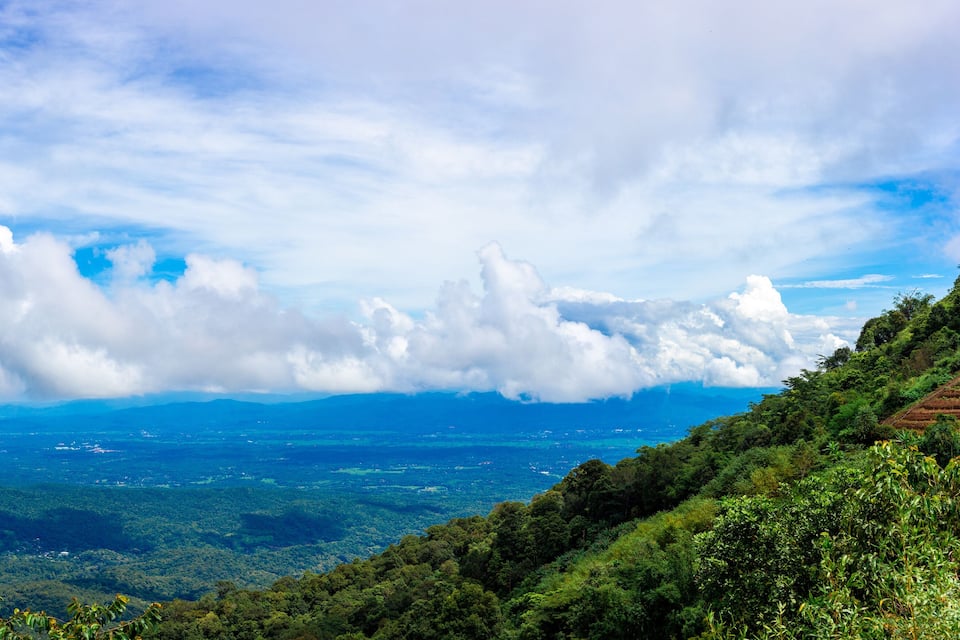 Paisagem montanhosa com florestas densas, céu claro e nuvens esparsas.