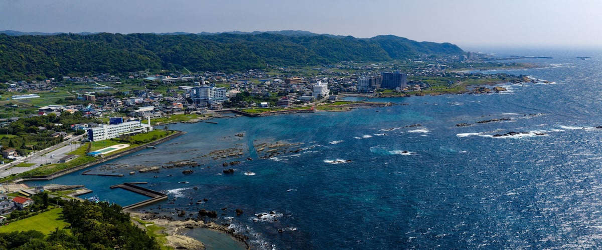 A coastal city with a river, buildings, and a forested hill in the background.