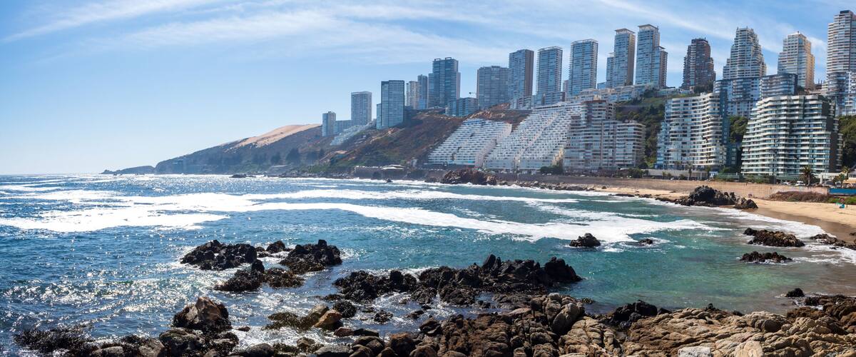 A coastal cityscape with high-rise buildings and rocky shoreline.