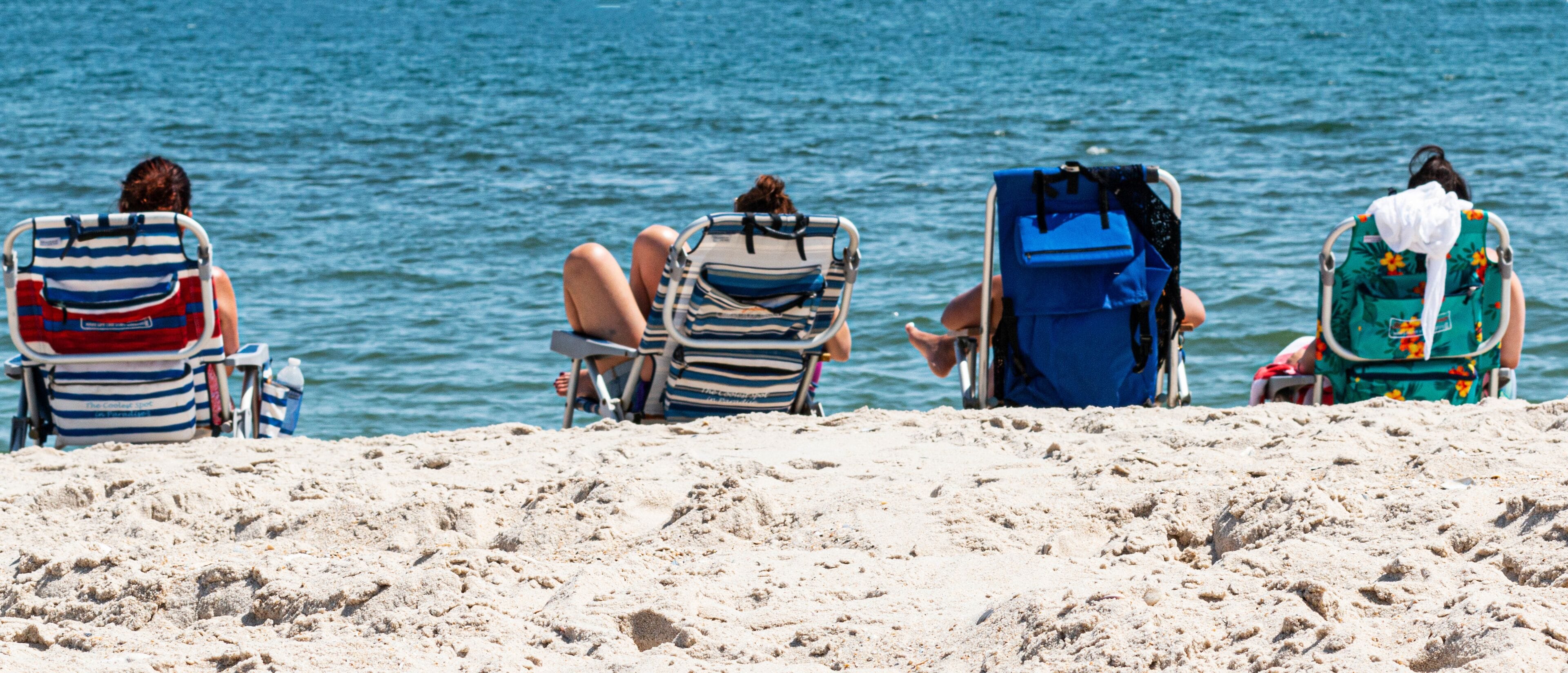 Three beach chairs facing the ocean, with sand in the foreground.