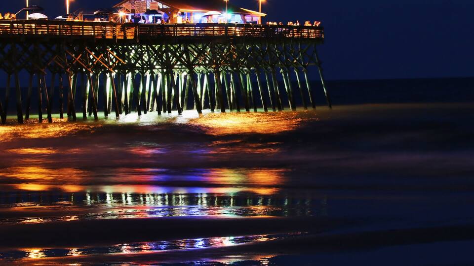 A pier extending into the water at night with reflections of lights on the water's surface.