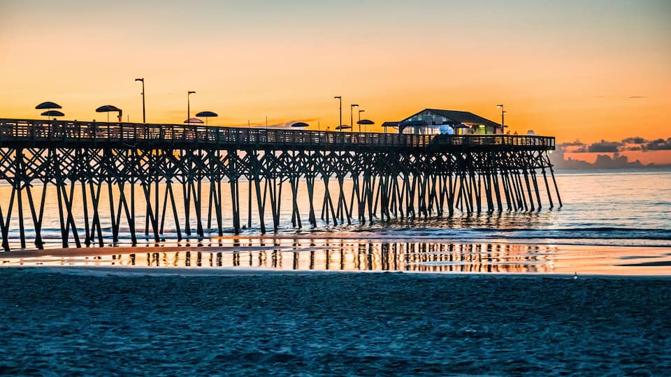A pier extending into the water with umbrellas and a building at the end.