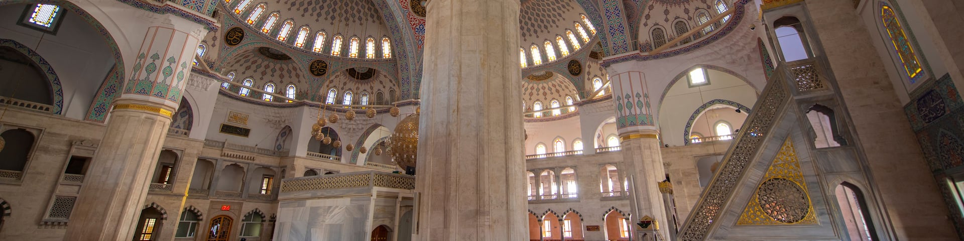 An ornate mosque interior with intricate tile work, large columns, and a red carpeted floor.