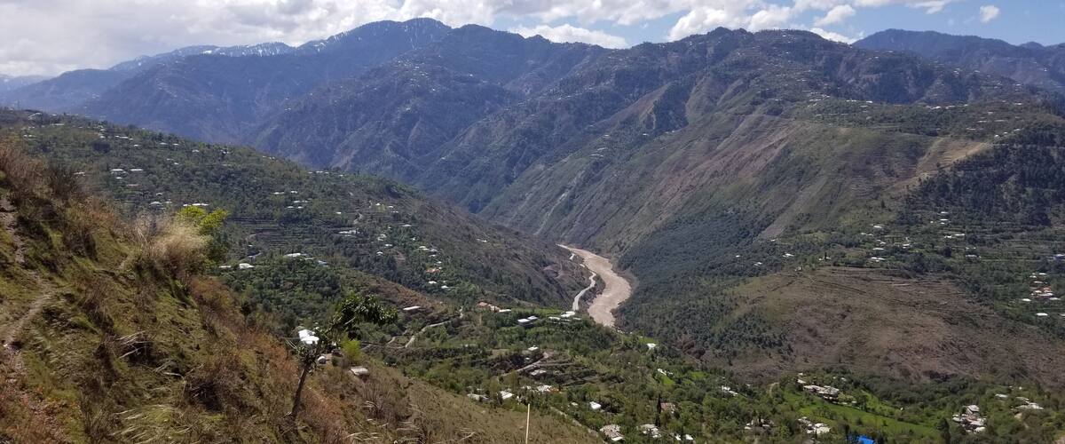 A valley with terraced fields, a winding road, and mountains in the background.