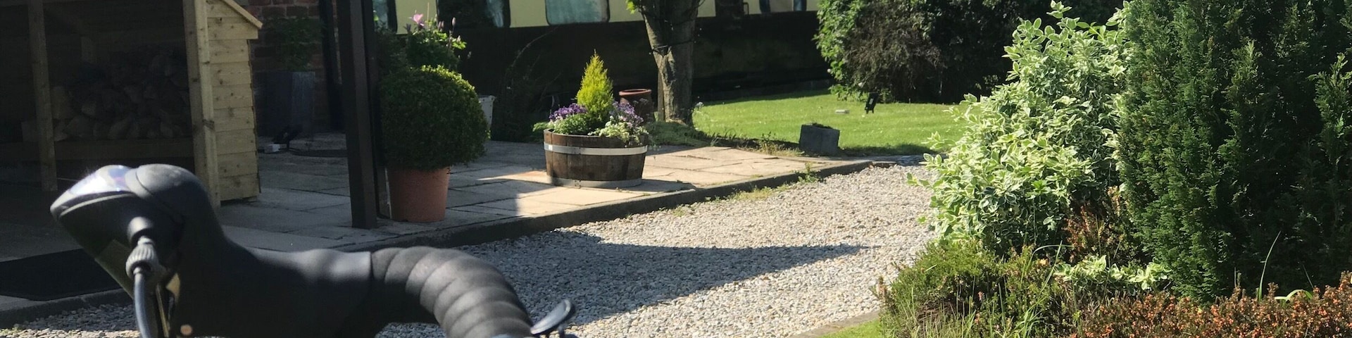 Ein Fahrrad in einem Garten mit einem Backsteingebäude, einem Baum und einem Kiesweg.