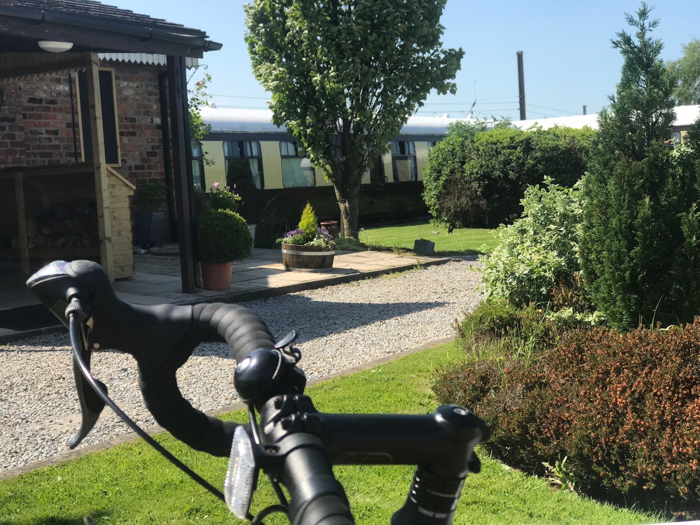 A bicycle in a garden with a brick building, a tree, and a gravel path.