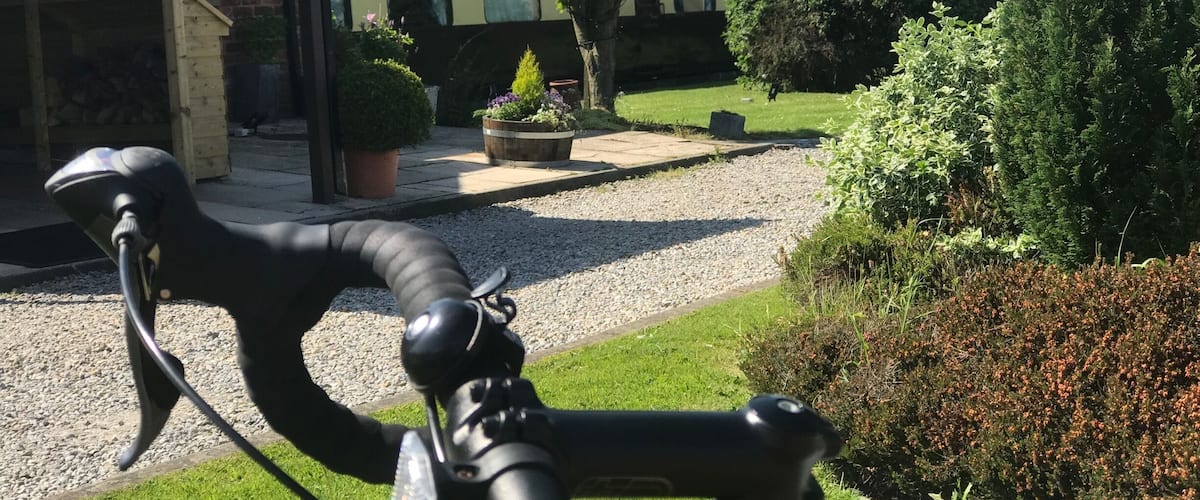 A bicycle in a garden with a brick building, a tree, and a gravel path.