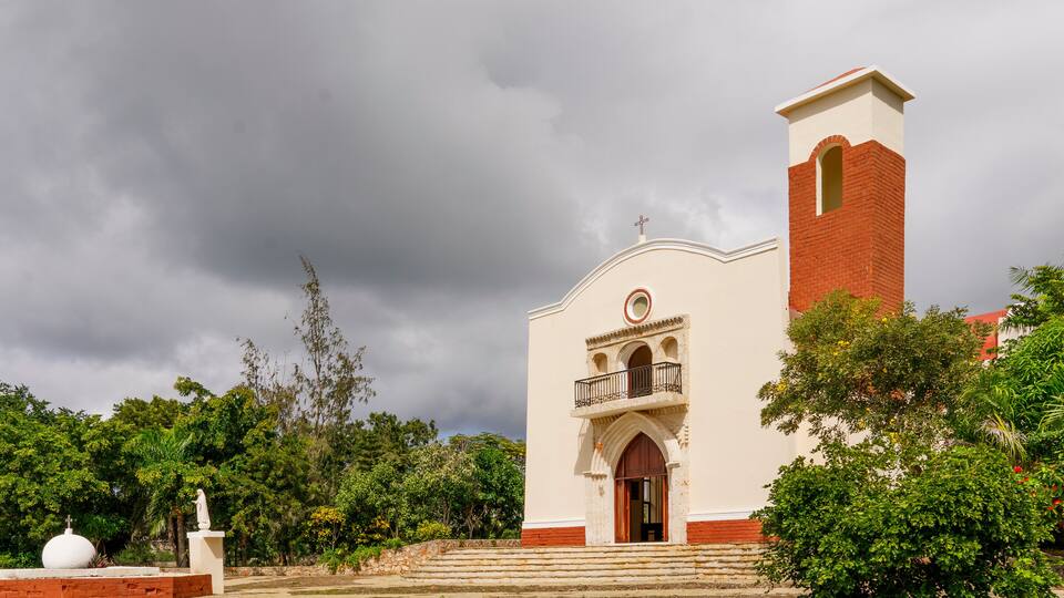 A church with a bell tower, surrounded by trees and a cloudy sky.