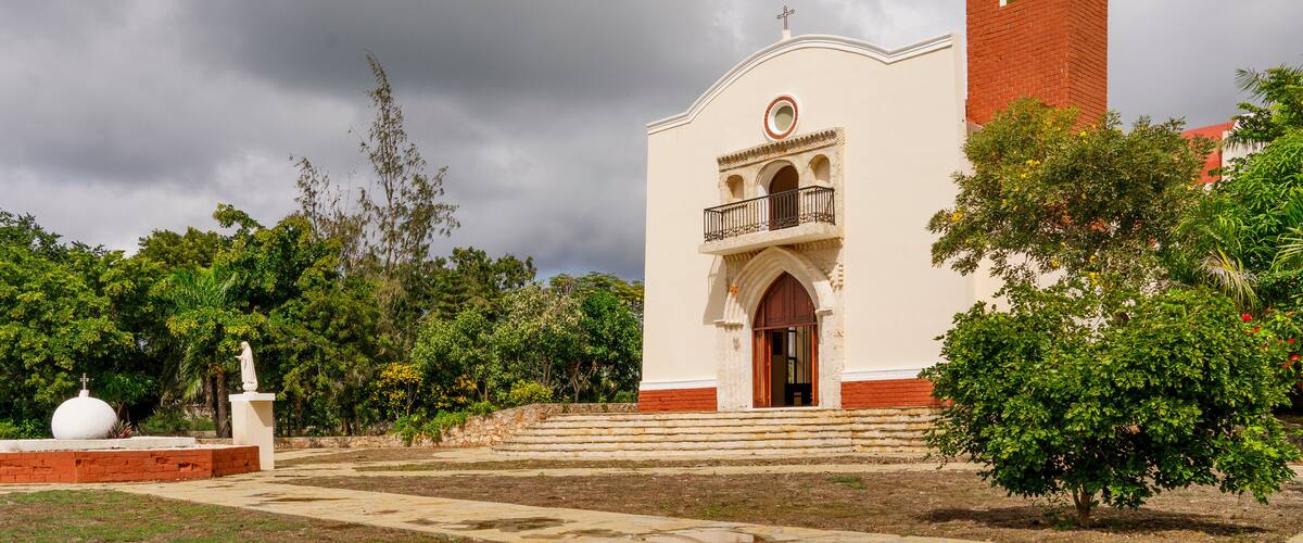 A church with a bell tower, surrounded by trees and a cloudy sky.