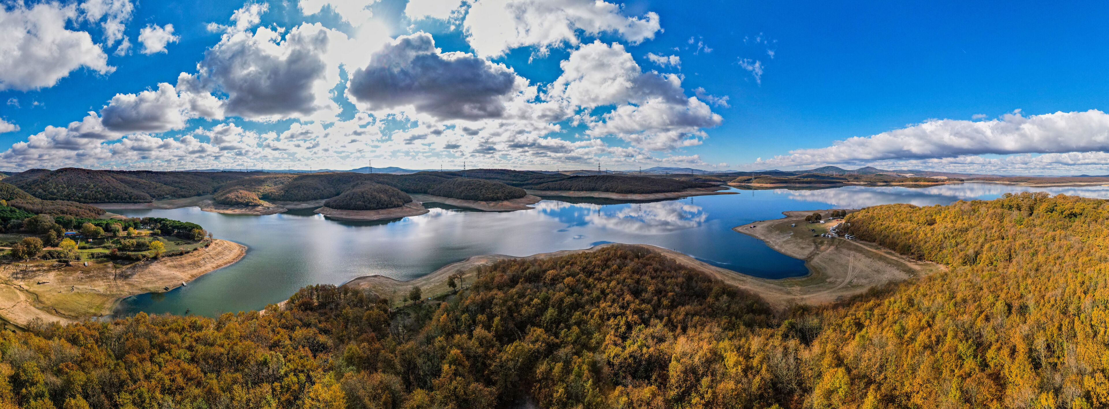 A lake surrounded by forested hills, a clear sky, and a few scattered clouds.