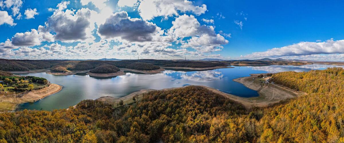 A lake surrounded by forested hills, a clear sky, and a few scattered clouds.