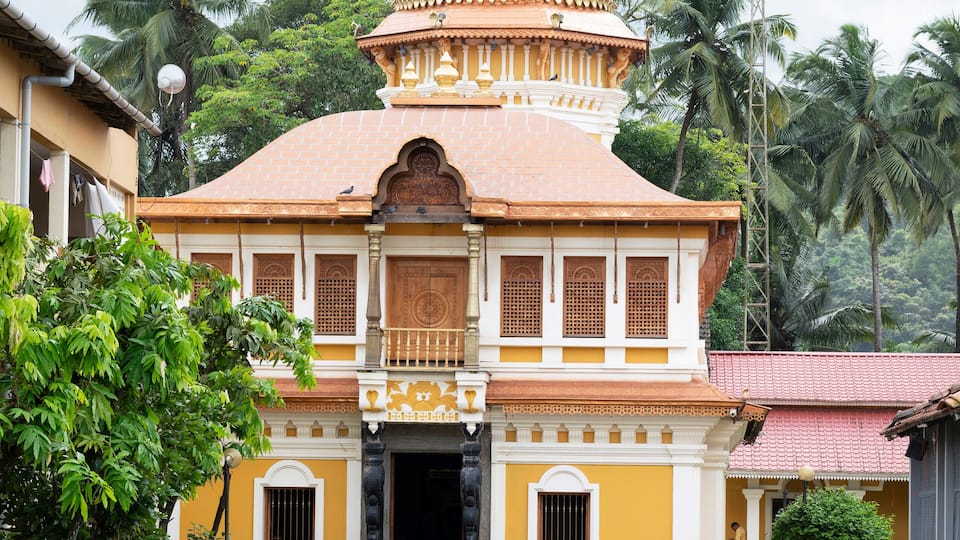 A traditional building with a dome and a red-tiled roof, surrounded by greenery and palm trees.