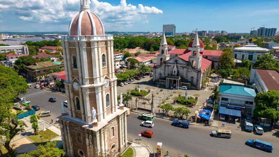 A historic church with a prominent dome and bell tower, surrounded by a bustling urban street with vehicles and pedestrians.