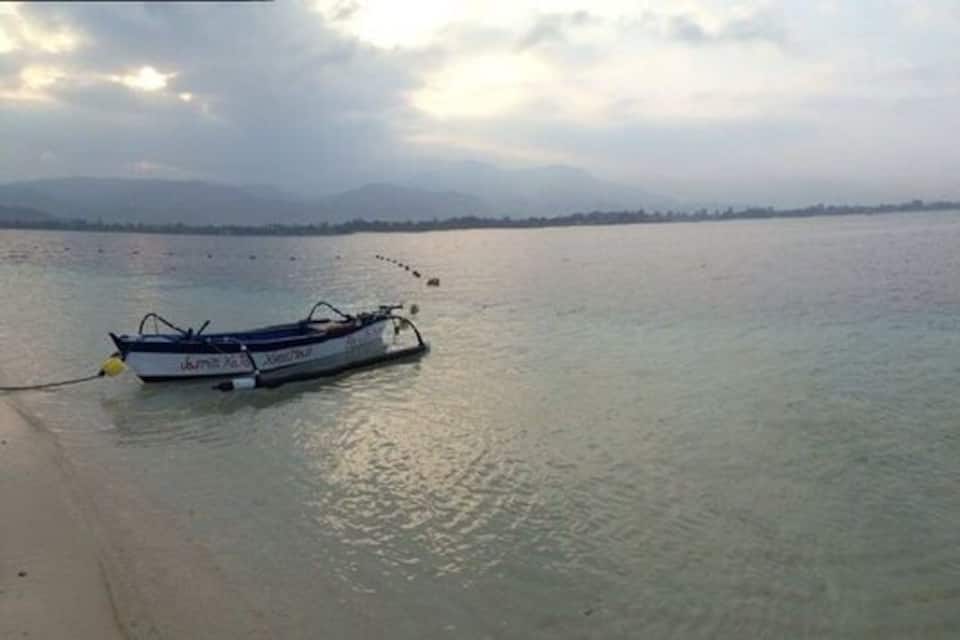 A boat on calm water near a sandy beach with a distant shoreline.