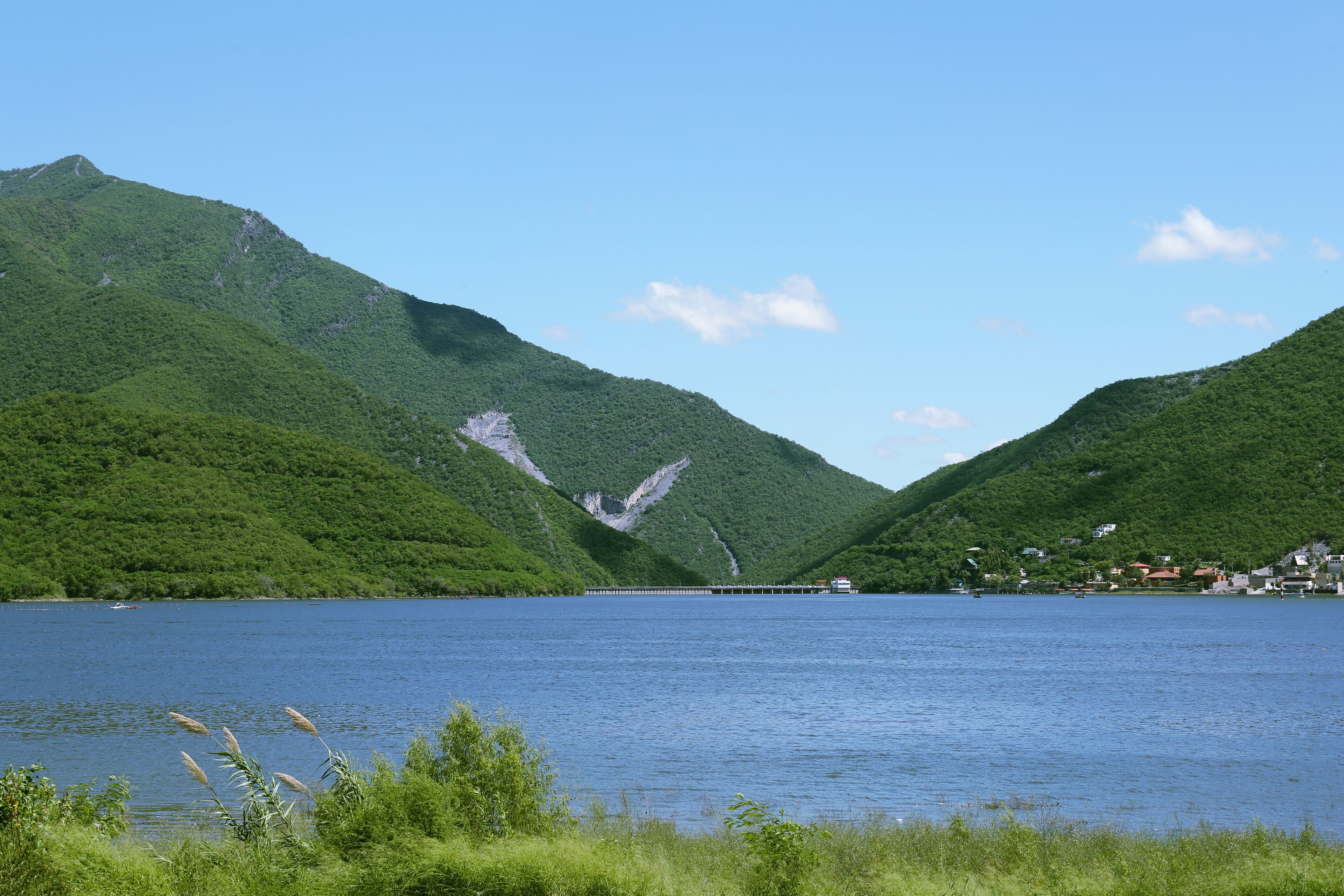 A lake surrounded by lush green hills, a pier extending into the water, and a small settlement on the right.