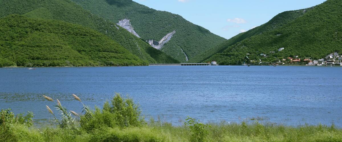 A lake surrounded by lush green hills, a pier extending into the water, and a small settlement on the right.