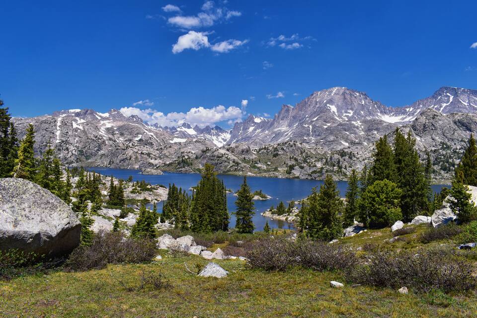 A mountainous landscape with a lake, rocky terrain, and evergreen trees.