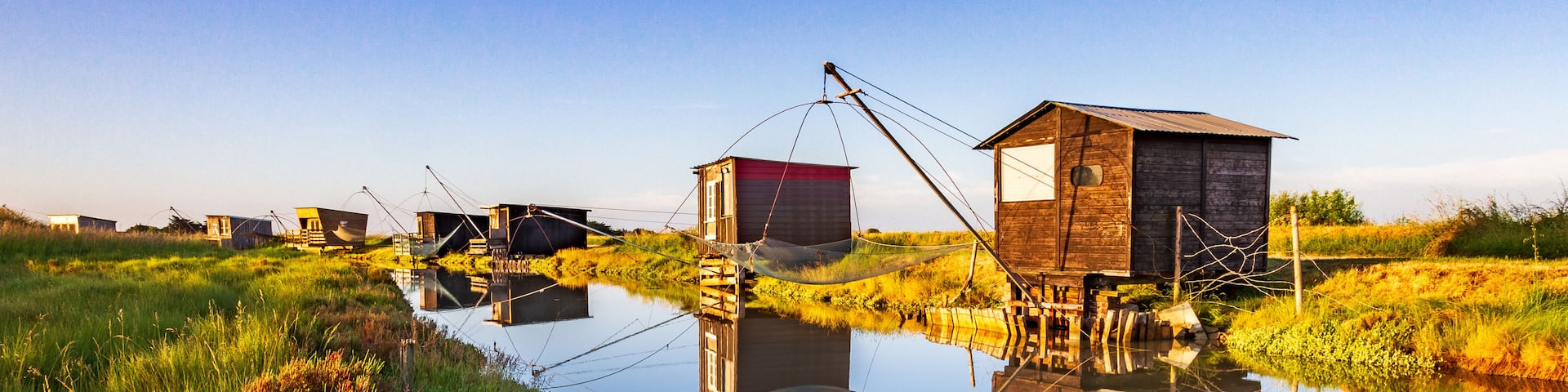 A calm river with wooden structures on stilts, surrounded by lush greenery.