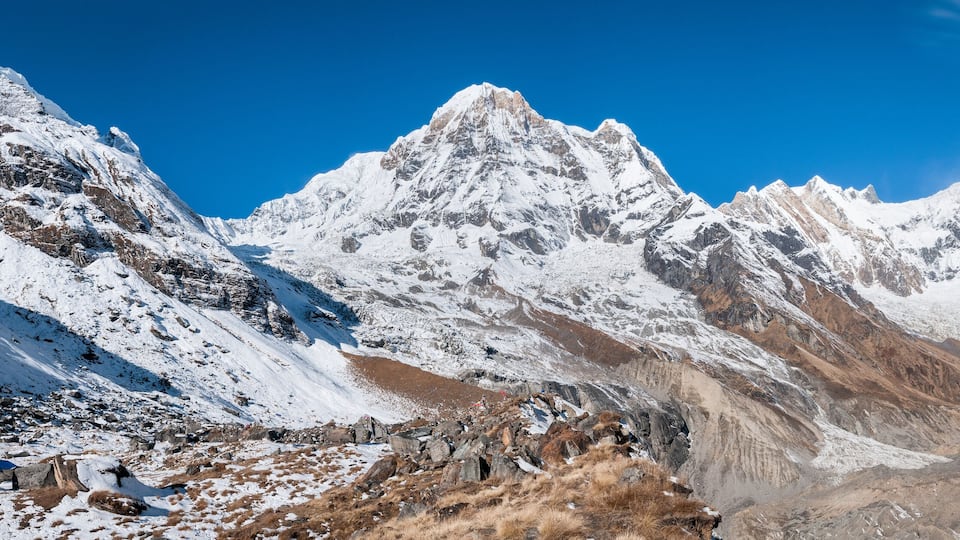 A snow-covered mountain range with rocky outcrops and a small hut.