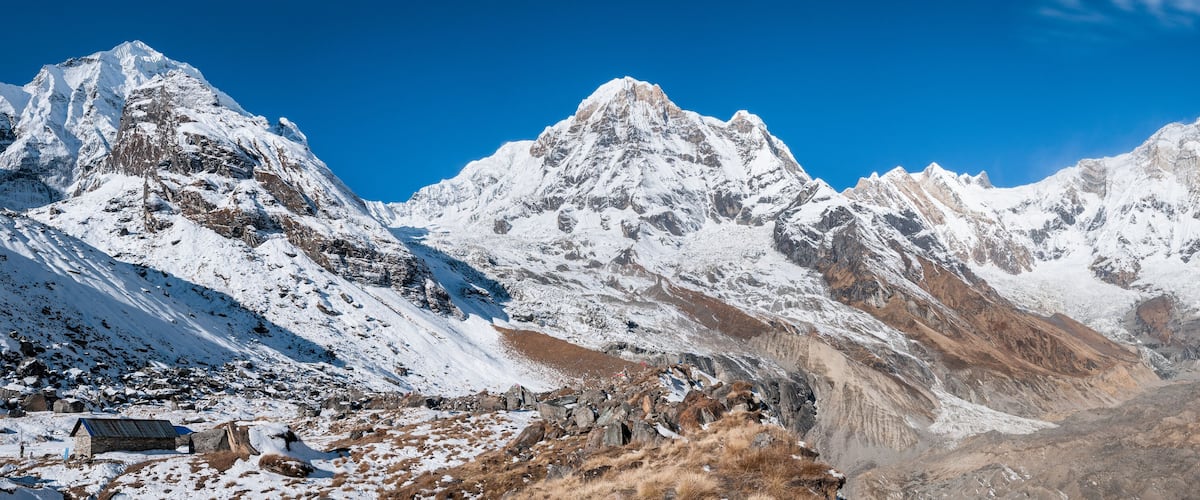 A snow-covered mountain range with rocky outcrops and a small hut.
