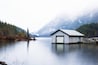 A wooden boathouse on a calm lake with a mountain backdrop.