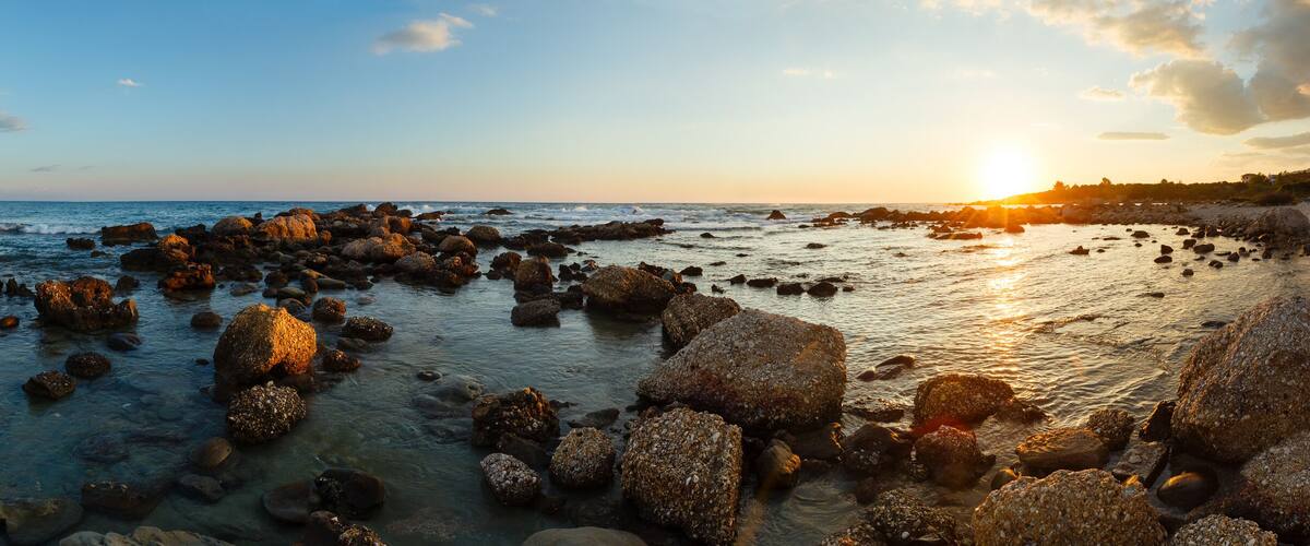 A rocky shoreline with the sun setting over the ocean.