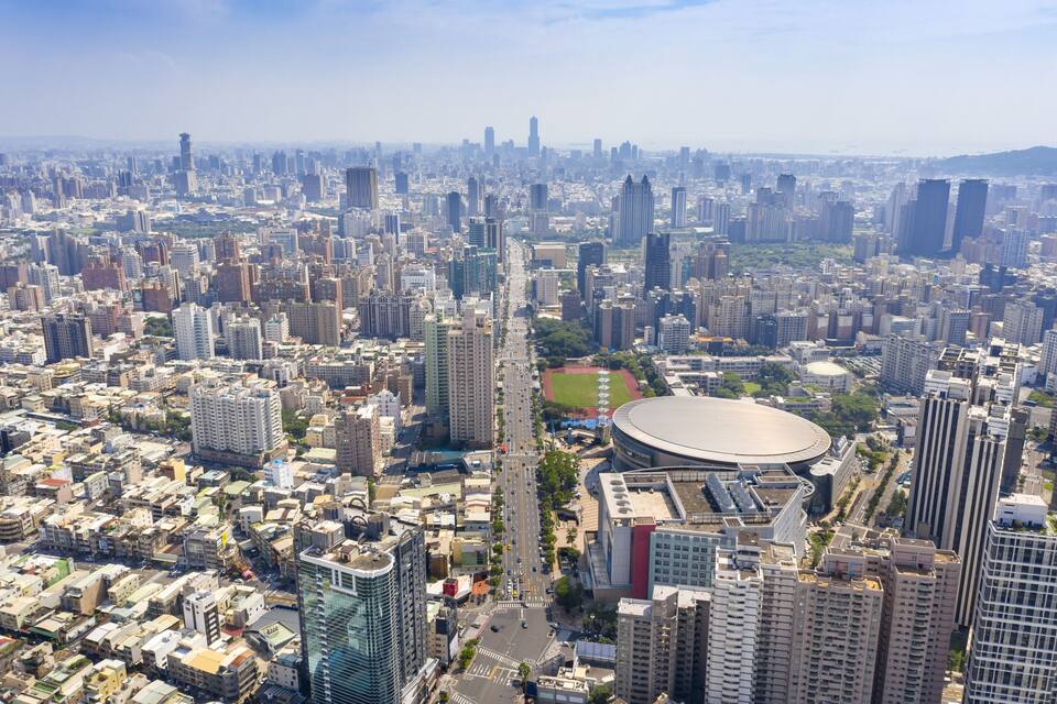 A densely populated cityscape with numerous high-rise buildings, a large stadium, and a sports field.