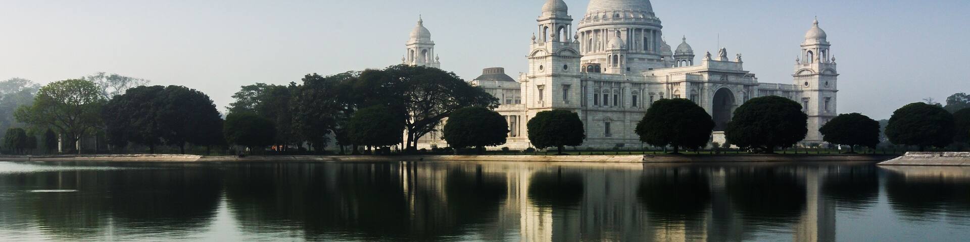 A large white building with domes and towers, reflecting in a calm body of water.