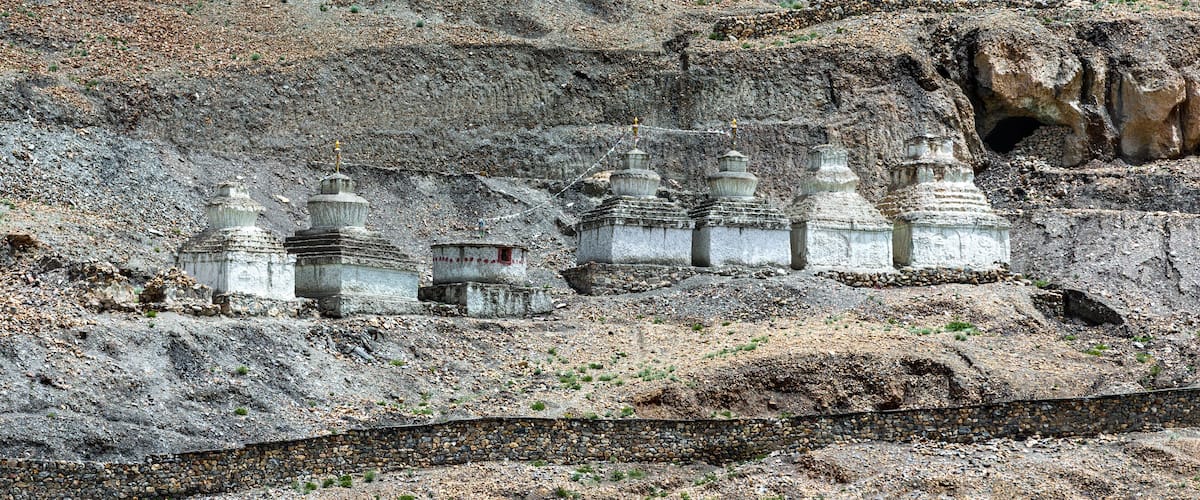 A series of white stupas on a rocky hillside.