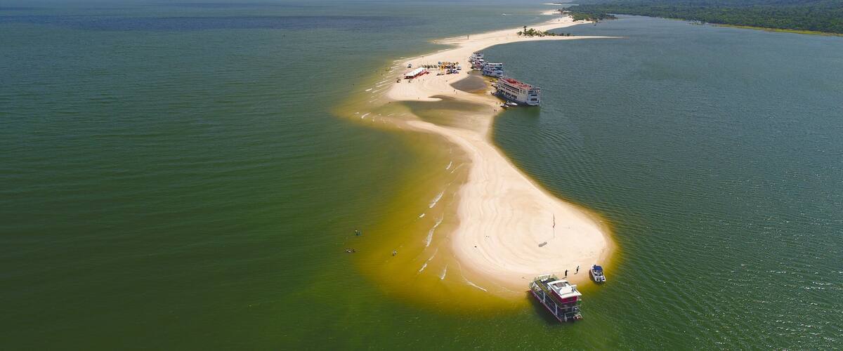 An aerial view of a beach with a boat docked on the shore, surrounded by calm waters and a distant shoreline.