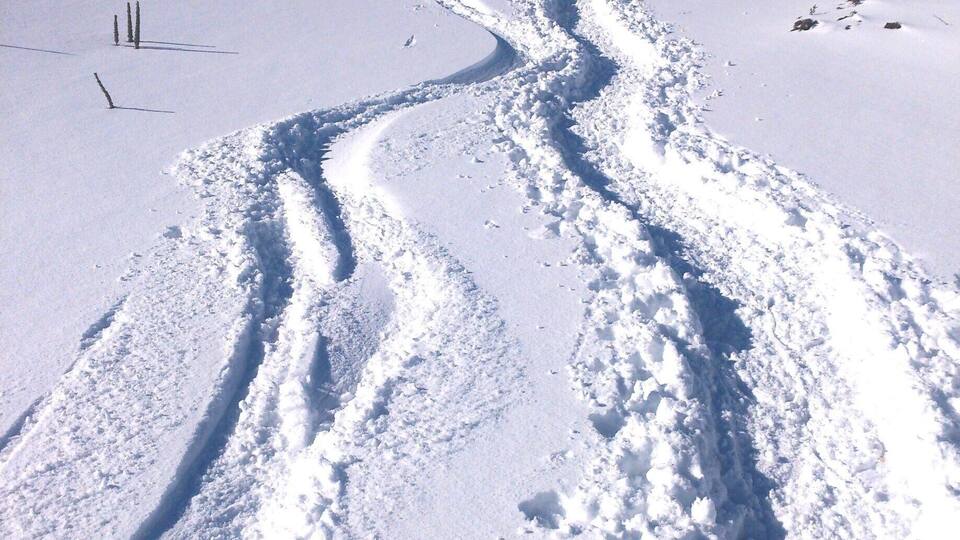 A snowy mountain trail with footprints and a clear blue sky.