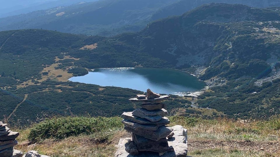 A stack of rocks on a hillside overlooking a lake with mountains in the background.