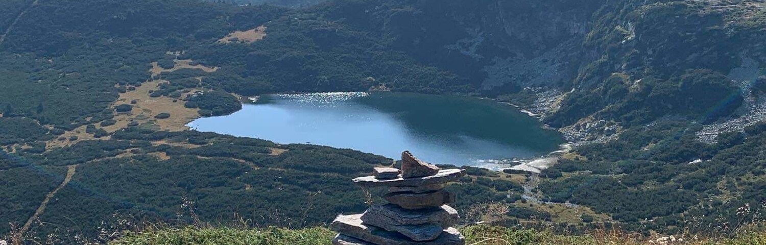 Una pila de rocas en una ladera con vistas a un lago y montañas al fondo.