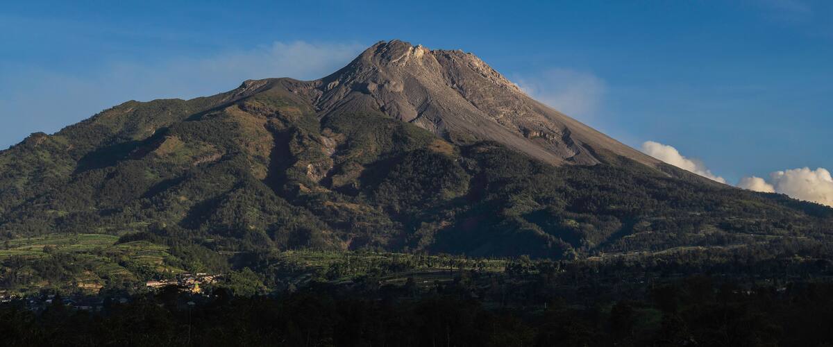 A mountain with a peak, surrounded by forested hills and a small village at its base.