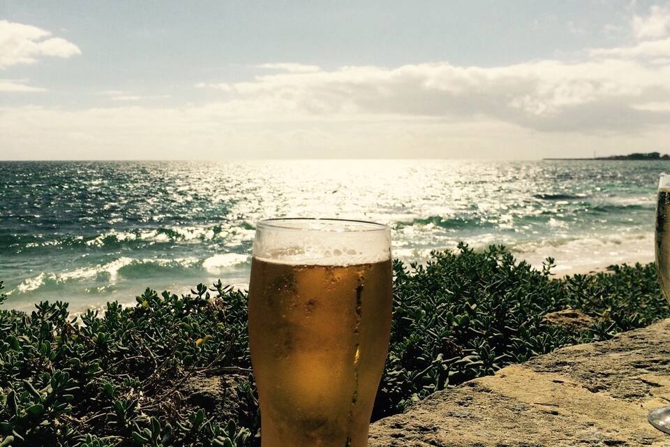 A glass of beer on a rock by the sea with waves in the background.