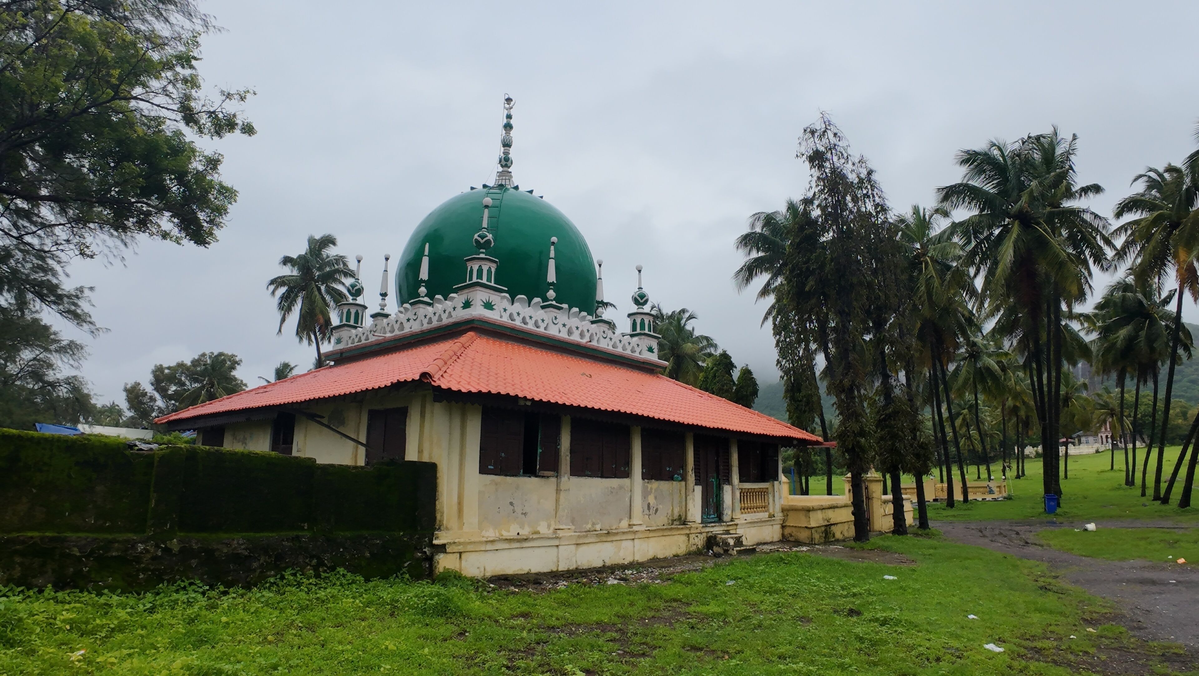 A green-domed building with a red roof, surrounded by palm trees and greenery.